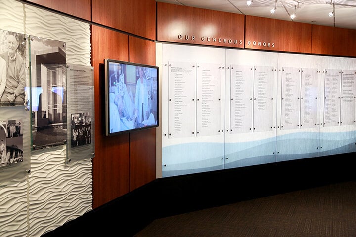 donor thank you wall with glass panels with lists of donor names and a television screen with a video still of a hospital patient